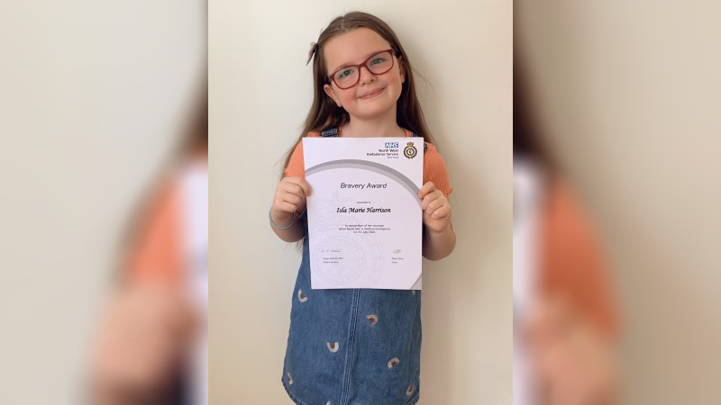 Six-year-old Isla holding up her Bravery Award certificate