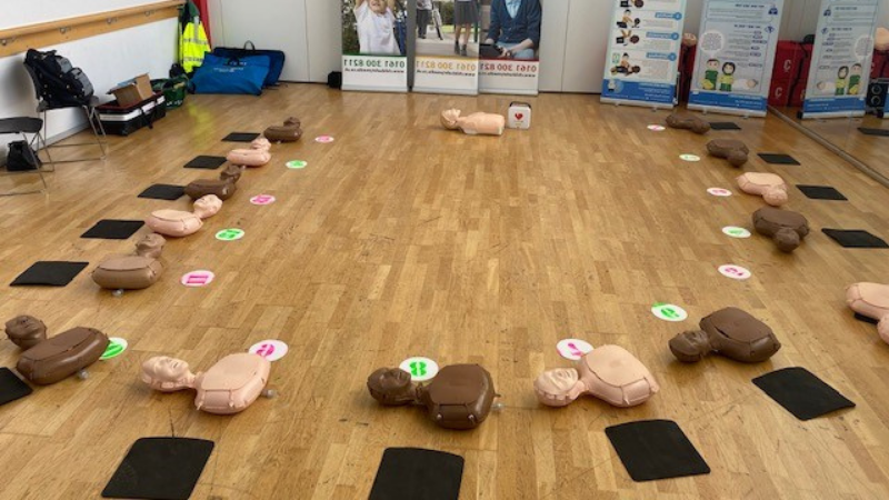 Resuscitation annie dolls in a circle on a faux wooden floor with knee pads next to them