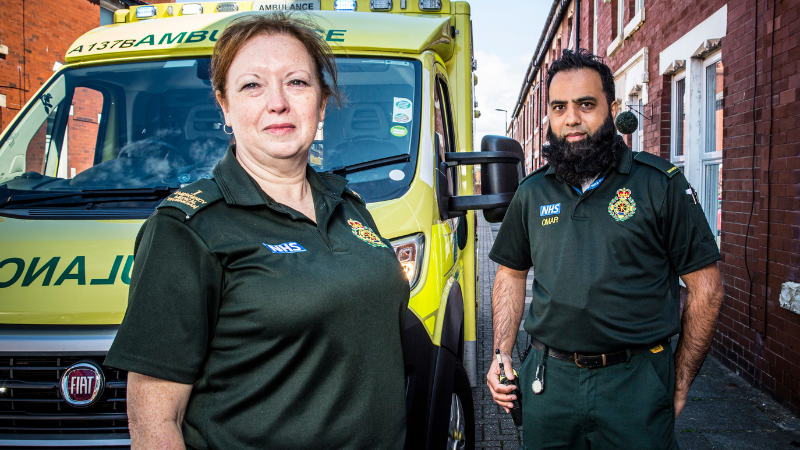 Male and female ambulance crewmates stood in front of ambulance.