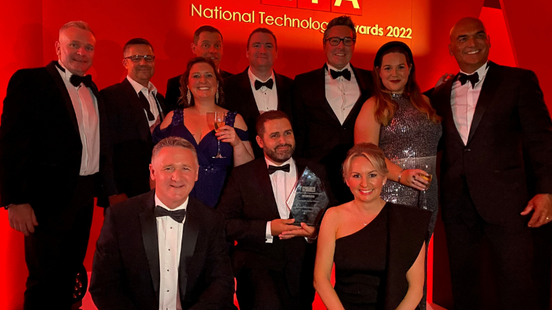 Staff celebrating holding award against a red backdrop at the National Tech Awards.