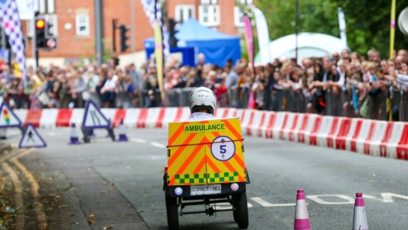 A Krazy Kart created by a team of NWAS ambulance crews competing in the Northwich Krazy Races. The Kart is shown from the back on a street with a big crowd of people in the background. 