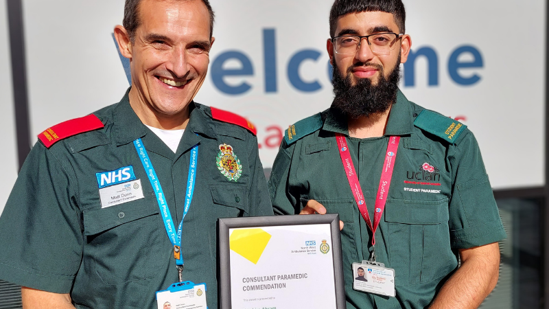 Consultant Paramedic Matt Dunn stood on the left presentitng the consultant paramedic commendation to Irabhim Akram. Both men are wearing green uniforms.