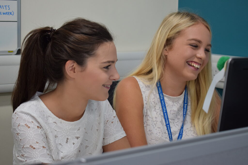 two female staff members smilling looking at a computer screen