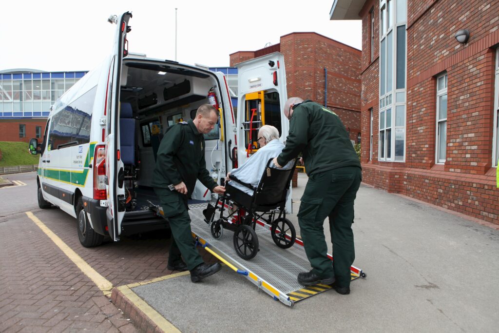 Ambulance staff pushing man in wheelchair in to ambulance.