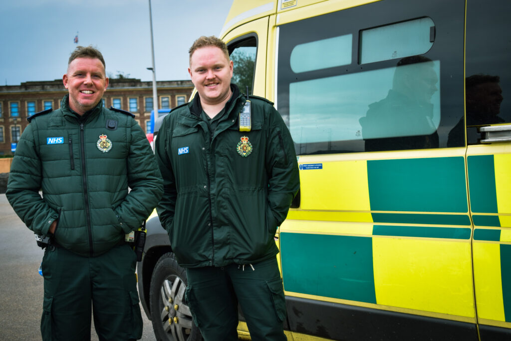 paramedic and emt smiling in front of ambulance vehicle 