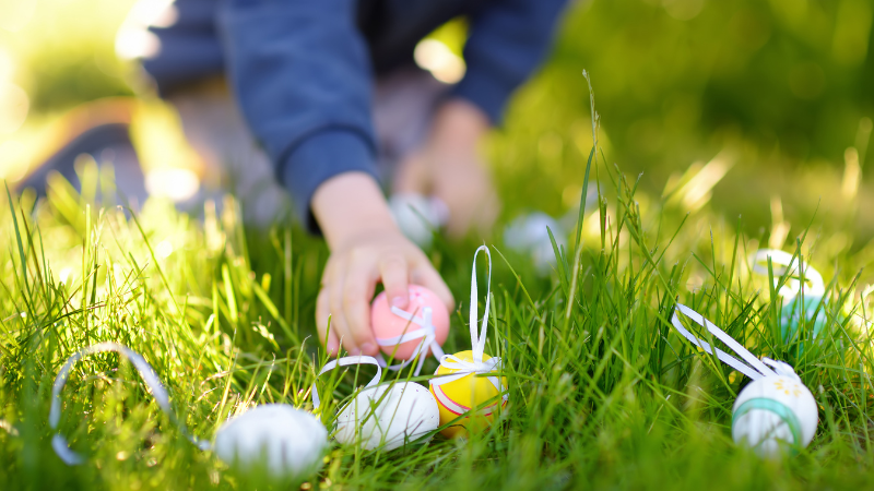 Easter eggs lying on the grass. An arm of a young child is picking one up.