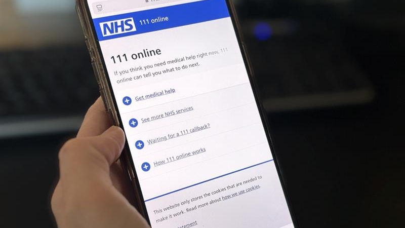 Hand holding a smartphone displaying the NHS 111 online webpage with options for medical help and services.