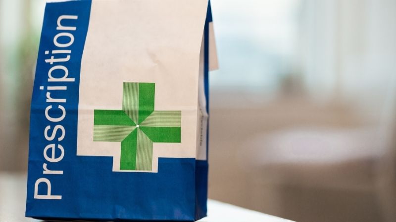 Prescription medication bag with a green cross, standing on a table.