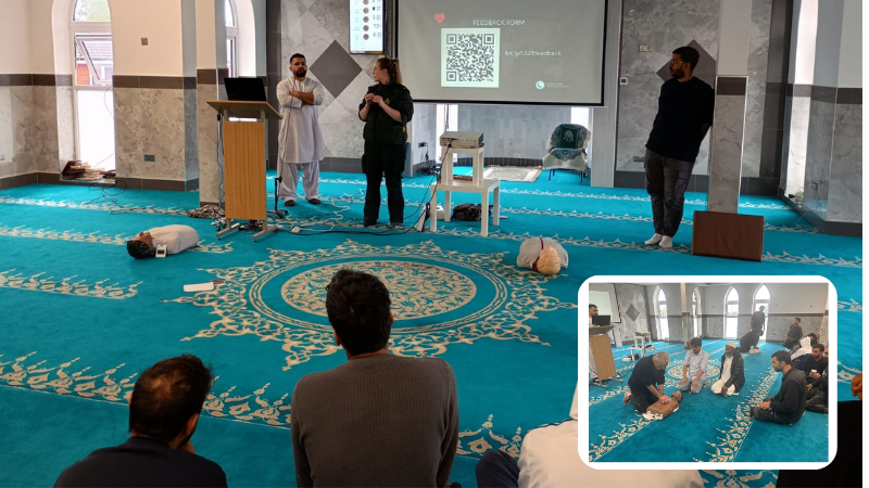 Two scenes from a first aid training session held in a mosque. In the main image, three individuals present a demonstration to an audience, with a QR code displayed on a screen. A smaller inset image shows participants practicing CPR on mannequins on the carpeted floor.