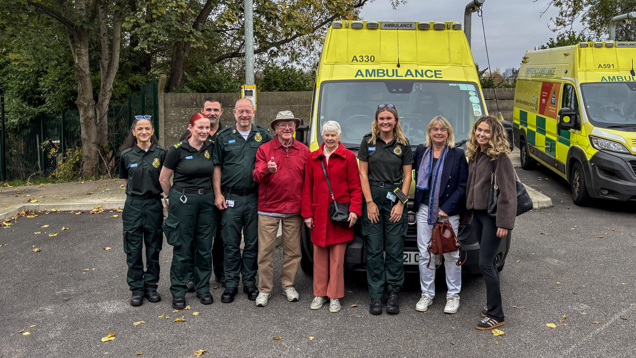 Group of eight individuals posing in front of an ambulance, with some wearing paramedic uniforms.