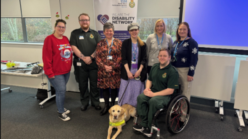 Photo of seven members of our staff disability network stood smiling in front of a promotional banner, including Netork Co-Chair Francesca (fourth-from-left) with her guide dog.