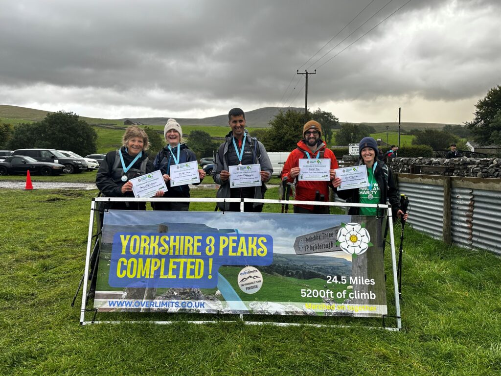 Group of people with medals and certificates standing in front of a Yorkshire Three Peaks sign
