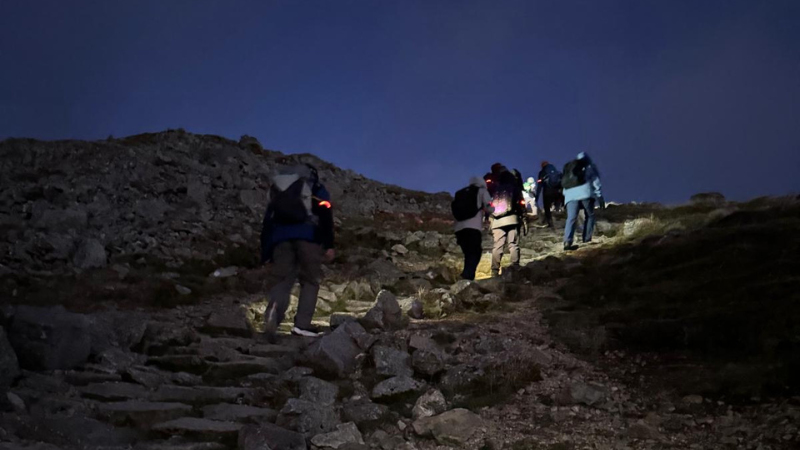 People trekking up a hill in the dark
