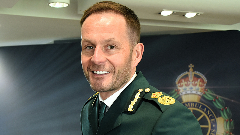 Head and shoulders image of Dan in his dark green dress ambulance uniform, smiling at the camera. 