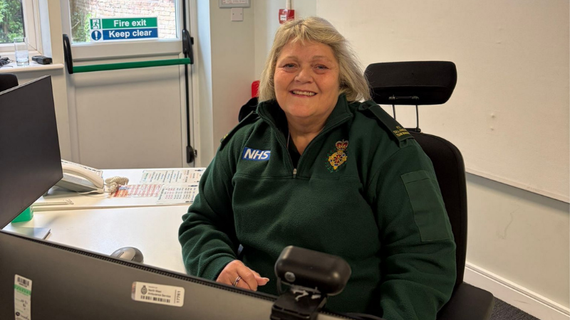 Suzanne sat at a desk smiling in her green uniform