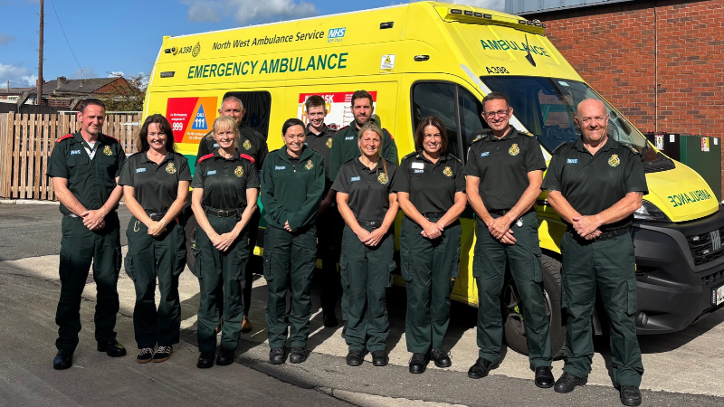 Group of ambulance staff standing in front of an ambulance and smiling at the camera