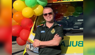 Adam stood infront of an ambulance that has balloons on it