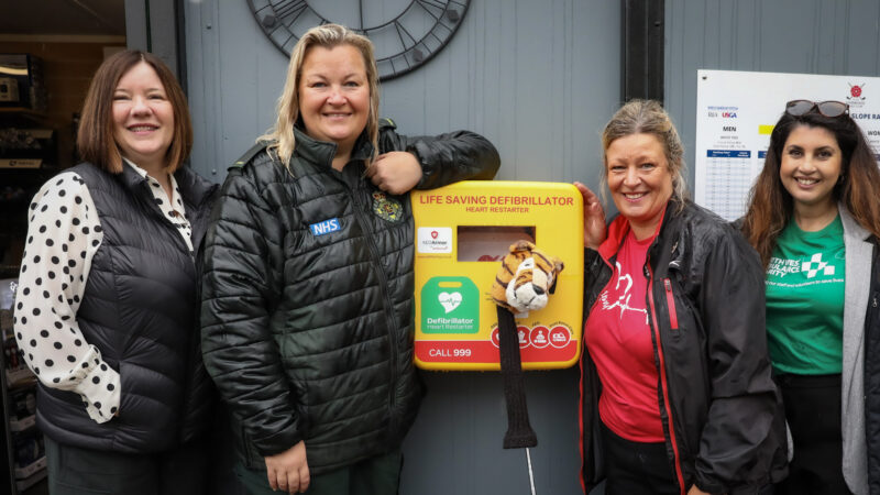 Three women stood in line with a defibrillator in the middle.