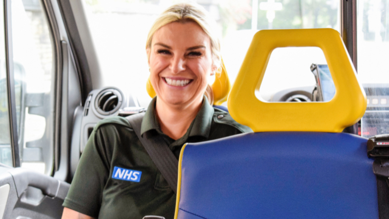 Female ambulance care assistant sat in the back of an ambulance smiling.