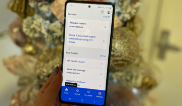 a hand holding a phone in front of a christmas tree displaying the NHS app