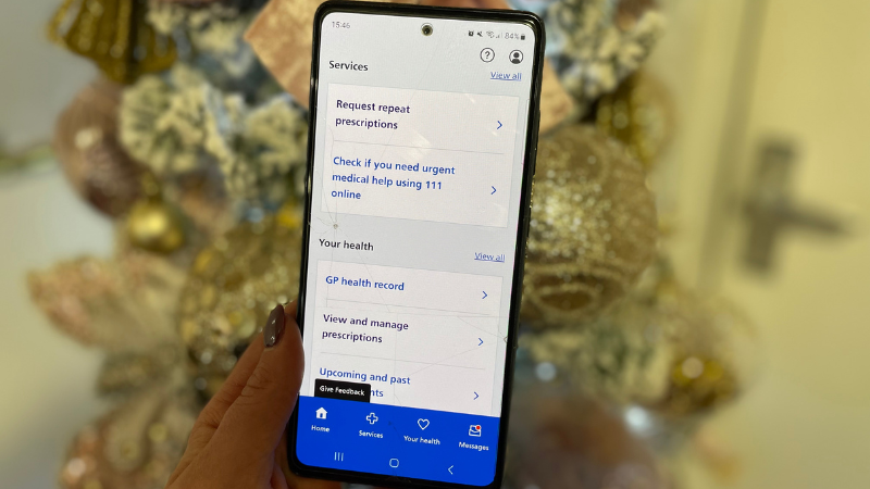 a hand holding a phone in front of a christmas tree displaying the NHS app