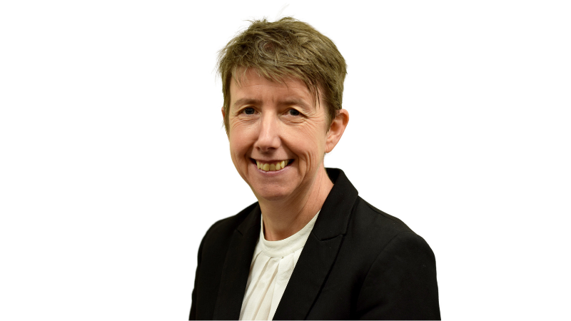 Portrait of a smiling individual with short hair, wearing a black blazer and a white shirt, against a plain light background.