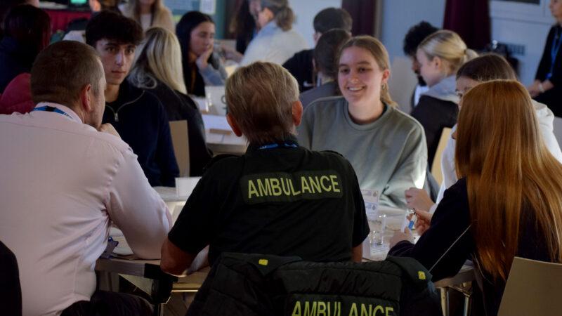 A group of people sat round a table in discussion, one with an ambulance uniform on.