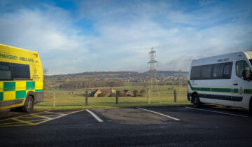 An ambulance and patient transport vehicle framing a rural landscape.