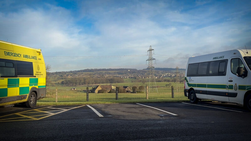 An ambulance and patient transport vehicle framing a rural landscape.