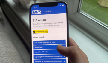 Hand holding a smartphone displaying the NHS 111 online help menu with options for medical assistance.
