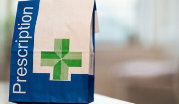 Prescription medication bag with a green cross, standing on a table.