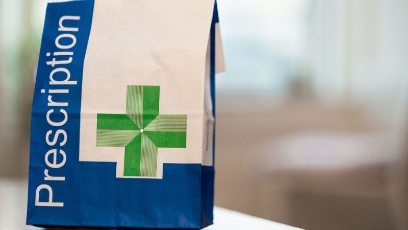 Prescription medication bag with a green cross, standing on a table.