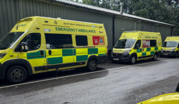 Three NWAS ambulance in a line front to back. There are lined up in front of a workshop building