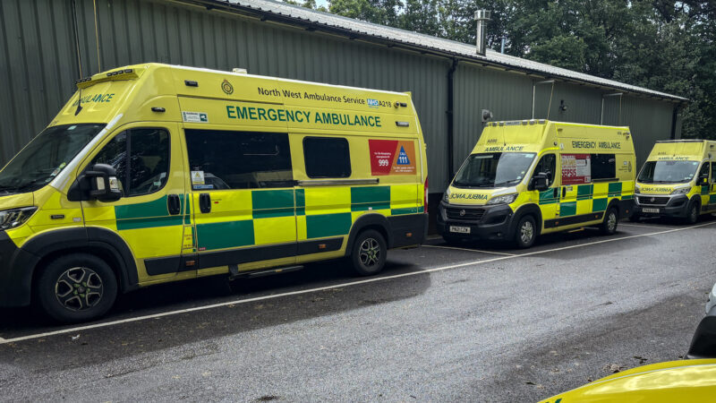Three NWAS ambulance in a line front to back. There are lined up in front of a workshop building
