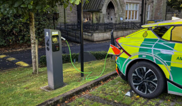 ambulance response vehicle plugged into an electric car charger in a car park in front large old looking house.