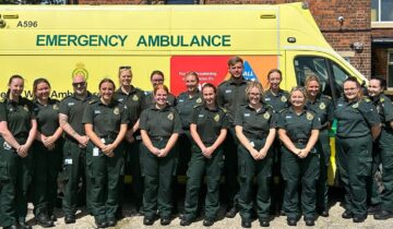Cohort of apprentice emergency medical technicians stood in front of an emergency ambulance