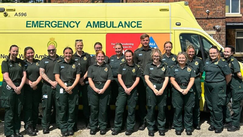 Cohort of apprentice emergency medical technicians stood in front of an emergency ambulance