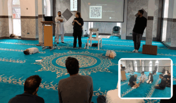 Two scenes from a first aid training session held in a mosque. In the main image, three individuals present a demonstration to an audience, with a QR code displayed on a screen. A smaller inset image shows participants practicing CPR on mannequins on the carpeted floor.