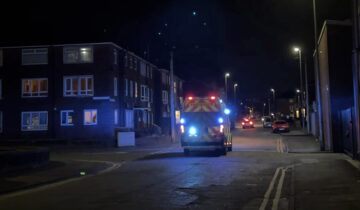 The bac of ambulance driving down a dark street at night time with it's blue lights on