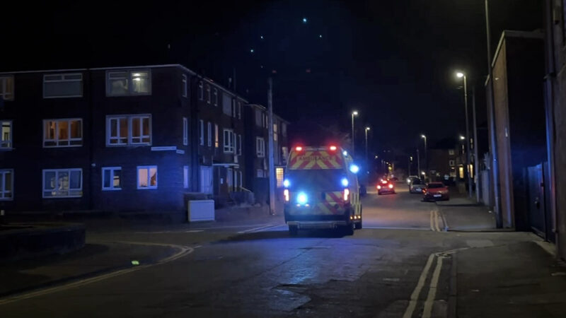 The bac of ambulance driving down a dark street at night time with it's blue lights on