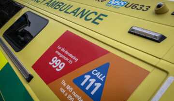 Close-up of an NHS ambulance sign with instructions: "For life-threatening emergencies CALL 999" and "The NHS number when it's not a 999 emergency CALL 111."