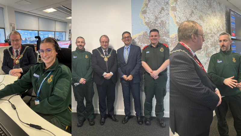 An office setting with several people interacting. One person is seated at a desk with computer screens displaying various data. Others, dressed in business attire and uniforms, are standing together. A large map and monitors showing information are visible in the background.