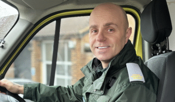Brian smiling at the camera sat in the cab of an ambulance.