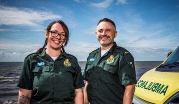 A man and a woman smiling. The right you see the bonnet of an ambulance