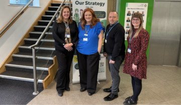 Four members of the Datix Team standing by a staircase with a banner in the background.