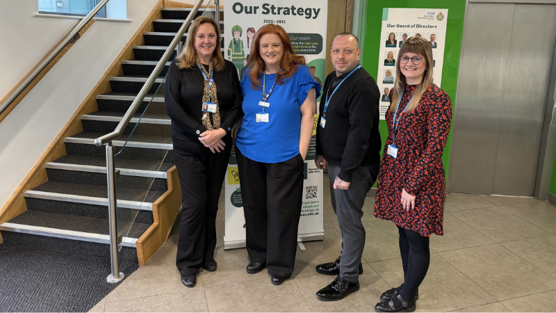 Four members of the Datix Team standing by a staircase with a banner in the background.
