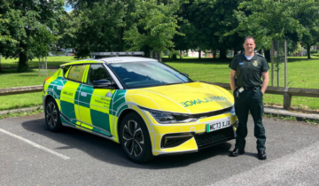 A man in green uniform stood to the side of an RRV. It is a sunny day.