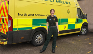 Singing Paramedic Cindy standing in her green uniform in front of an ambulance.