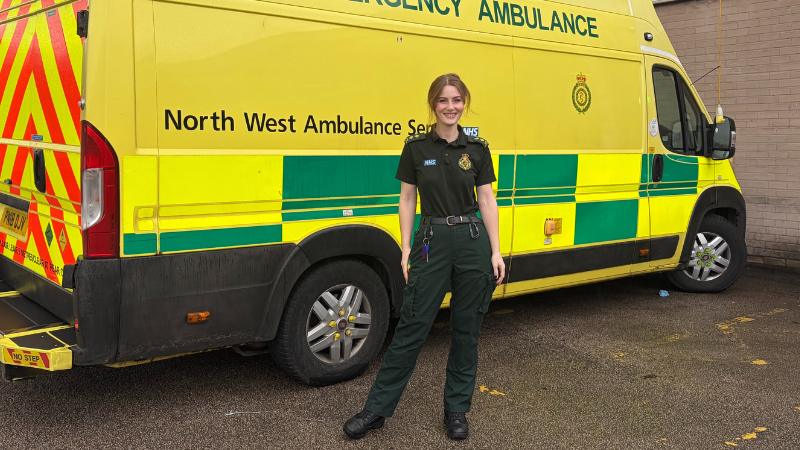 Singing Paramedic Cindy standing in her green uniform in front of an ambulance.
