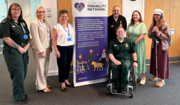A group of seven people, some in uniform, others in office attire, posing in front or by the side of a disability network banner